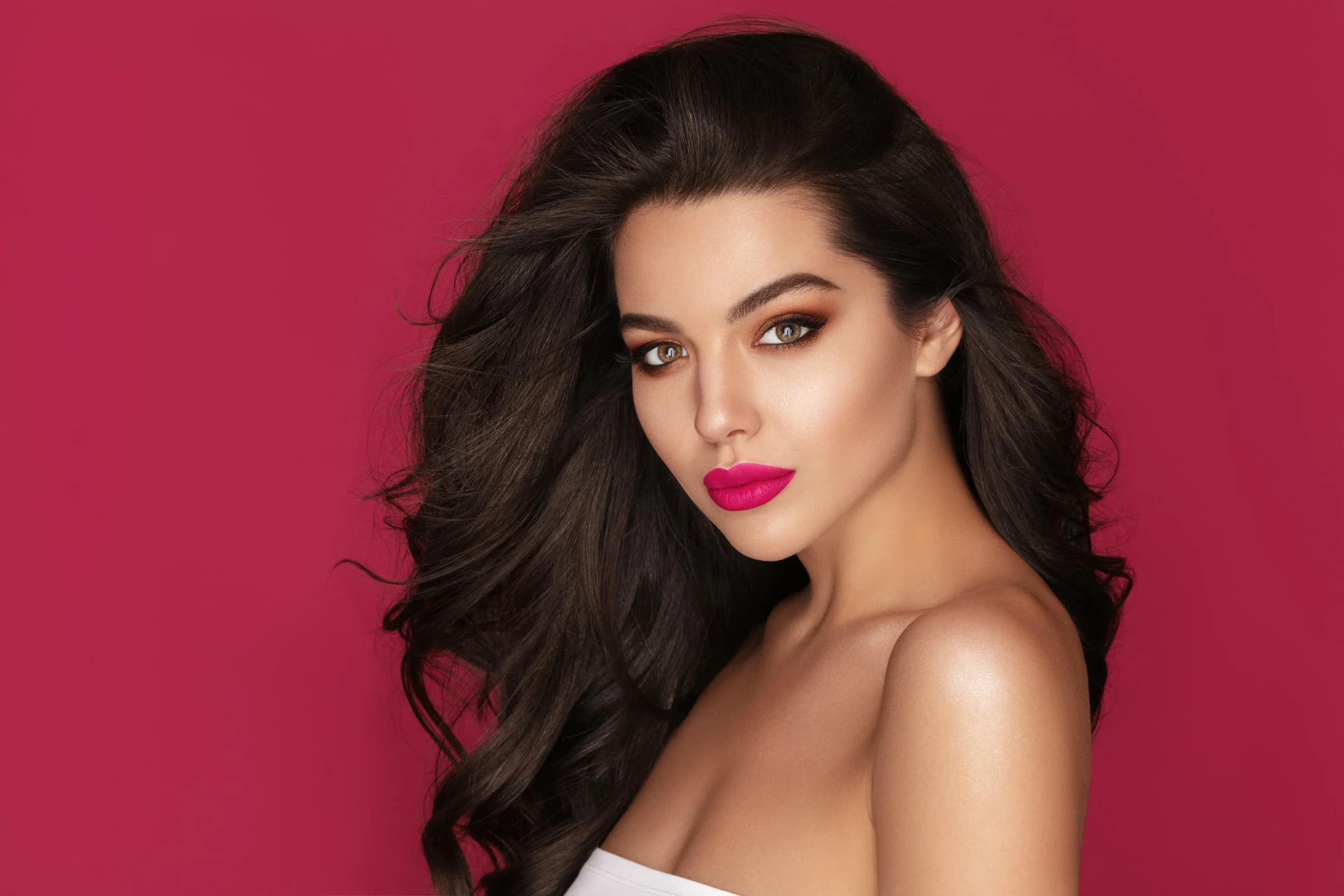 Woman with voluminous dark hair and bold pink lips against a magenta backdrop